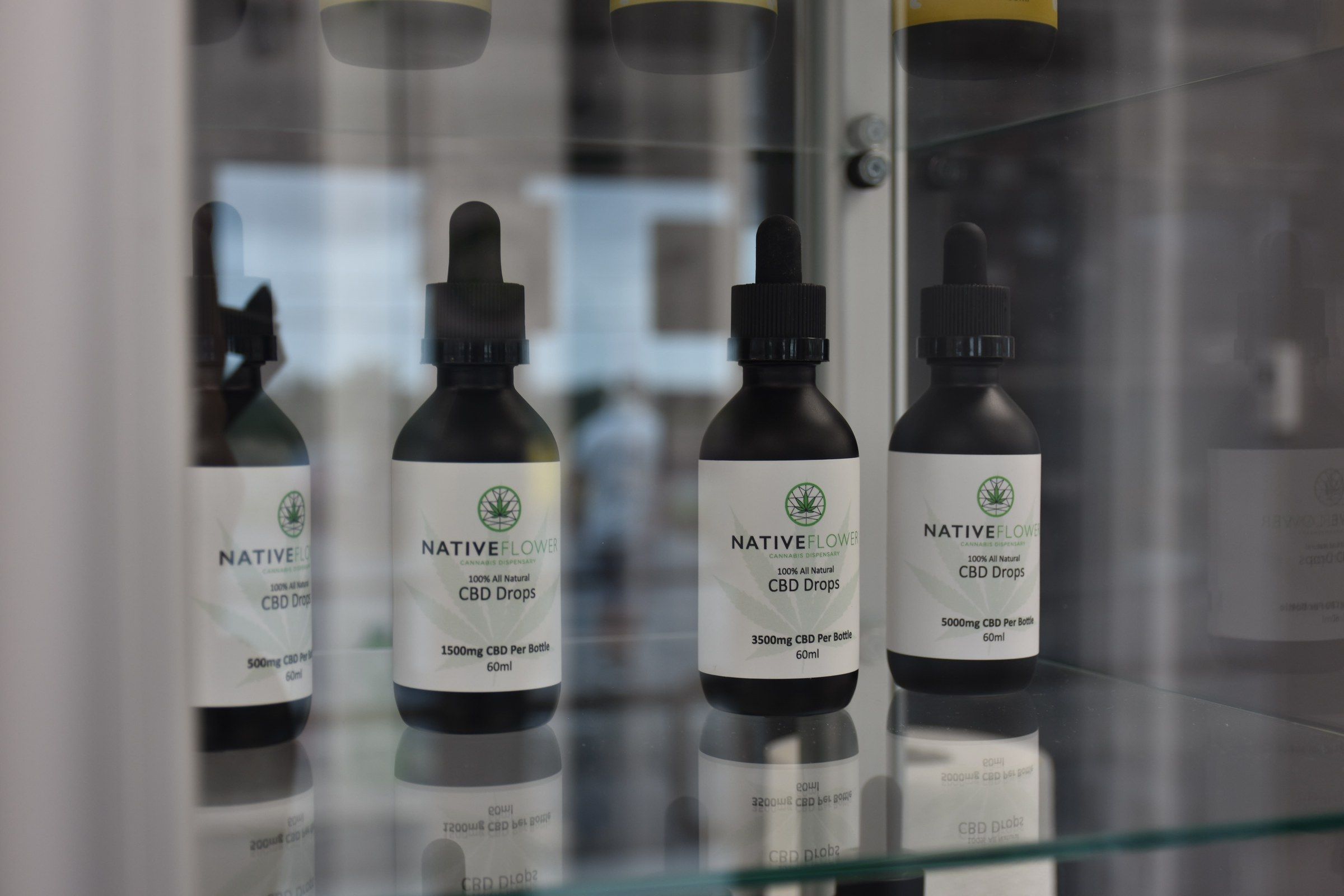 Four bottles of Native Flower CBD drops standing in a lit glass display case.