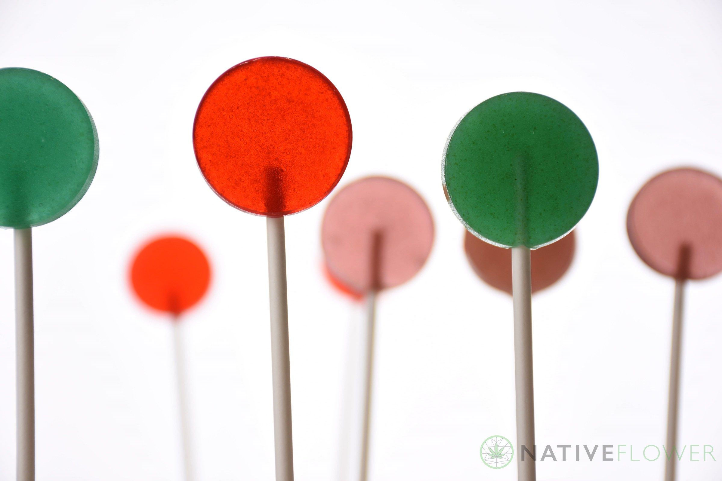 Cannabis lollipops in red, pink and green laid out on a white surface.